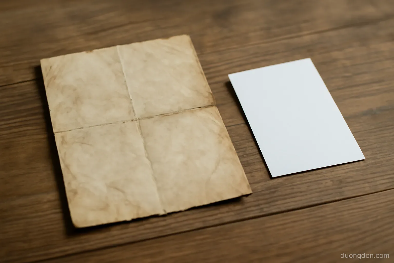 an old worn paper document with folded creases lying on a table beside a newer card, natural light, text not legible